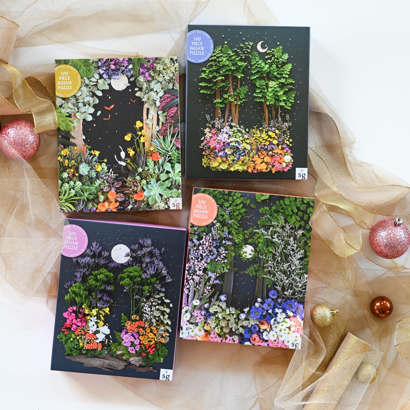 Four decorative boxes with nature-themed designs on a white background with sheer fabric and small ornaments.