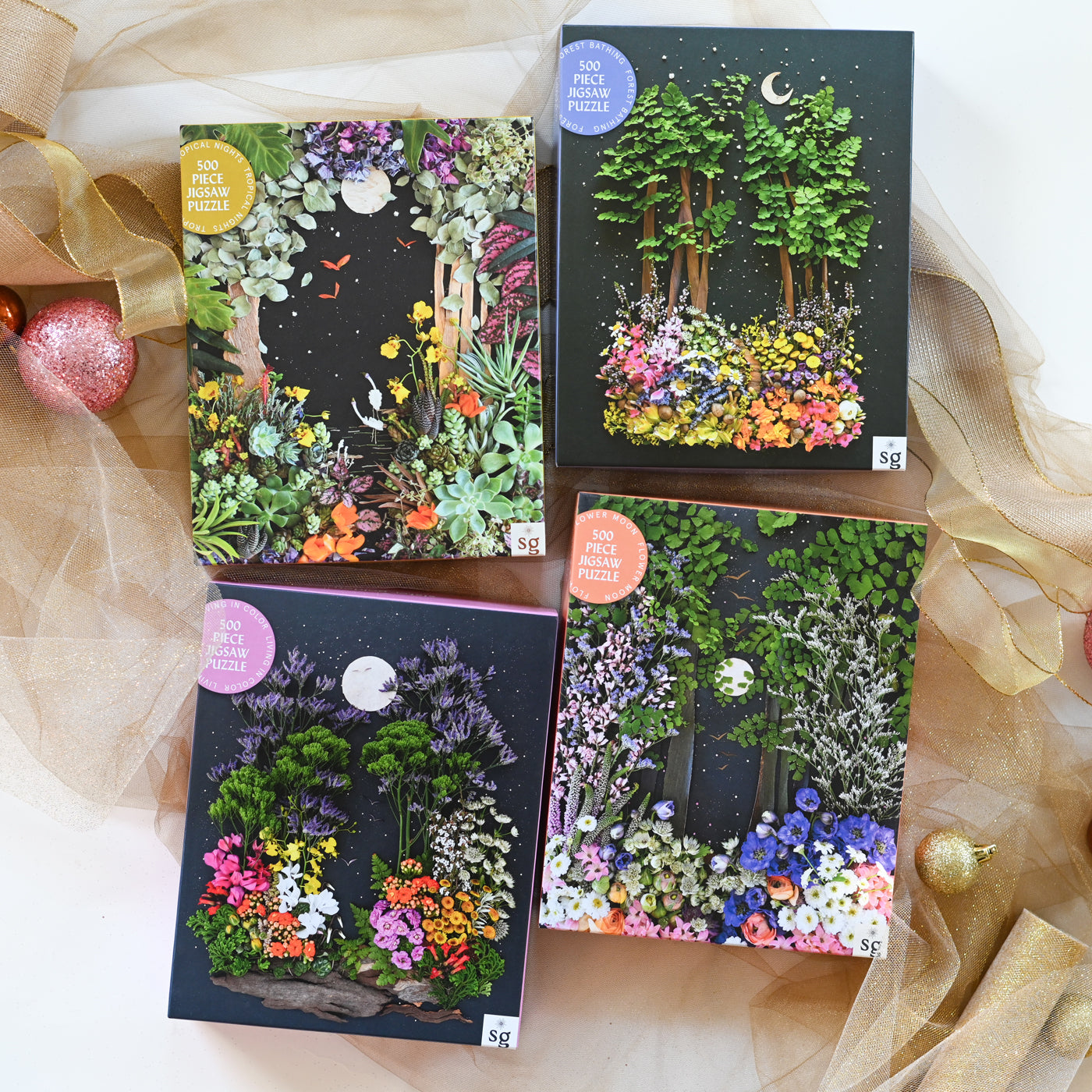 Four decorative boxes with nature-themed designs on a white background with sheer fabric and small ornaments.